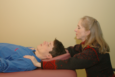 reiki practitioner placing her hands on the shoulders of a client, who is lying down