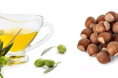 Container of oil and small pile of nuts on a white background