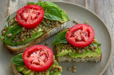 plate holding three pieces of whole-grain bread with avocado, basil, nuts, and tomato on top