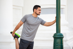 man leaning against a pole outside and stretching his leg before running