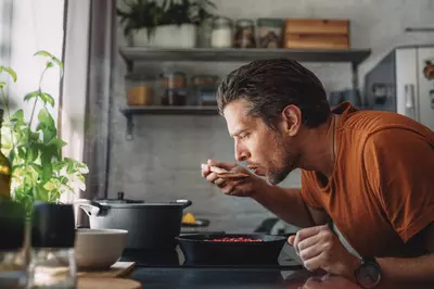 man tasting sauce from a cast iron pan