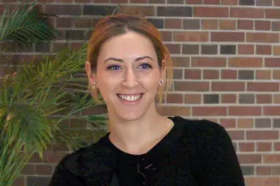 Kelly Mcgonical smiling at the camera in front of a brick wall