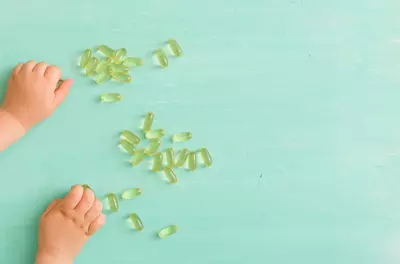 child's hands next to fish oil pills on turquoise background