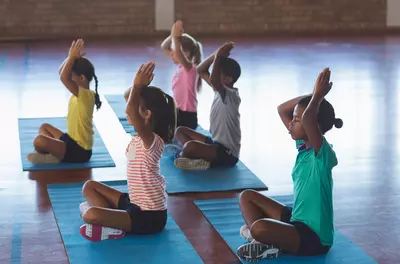 Group of five children doing yoga poses in a gym