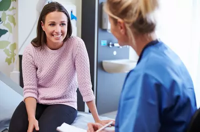 young woman sitting on hospital bed and smiling as she talks to a nurse