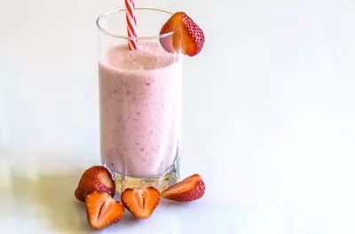 pink smoothie in glass surrounded by a few strawberries