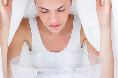 woman with a towel draped over head, inhaling steam from a bowl