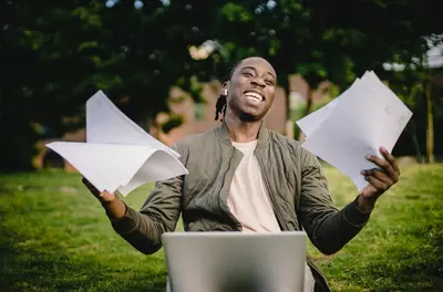 man smiling with papers and computer in lap